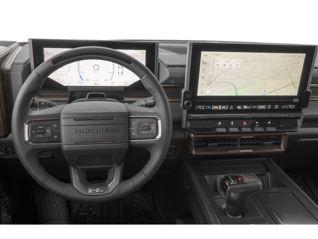 Close up view of 2026 GMC Hummer EV Pickup front dashboard from the drivers point of view. Steering wheel, temperature controls, gear shift and touch screen are visible.