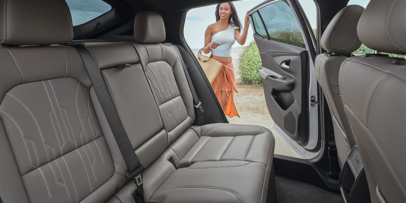 Woman on the beach opening the passenger door of the Buick Envista, back row of seats are visible