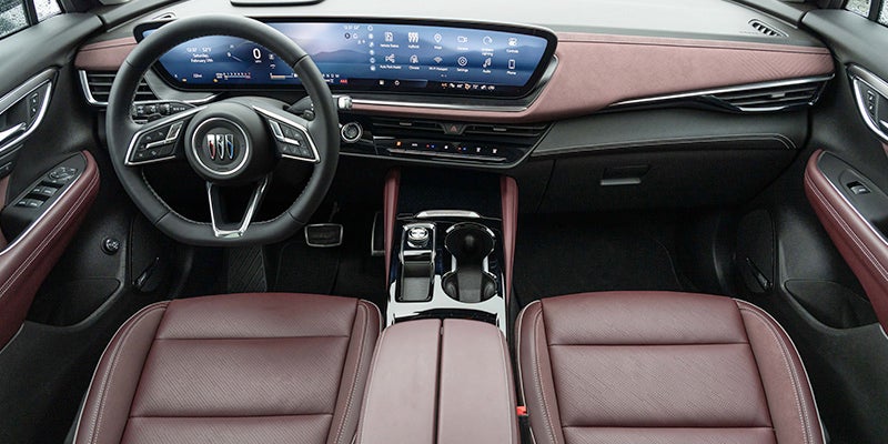 Close up view of 2025 Buick Envision front dashboard from the drivers point of view. Steering wheel, temperature controls, gear shift and touch screen are visible.